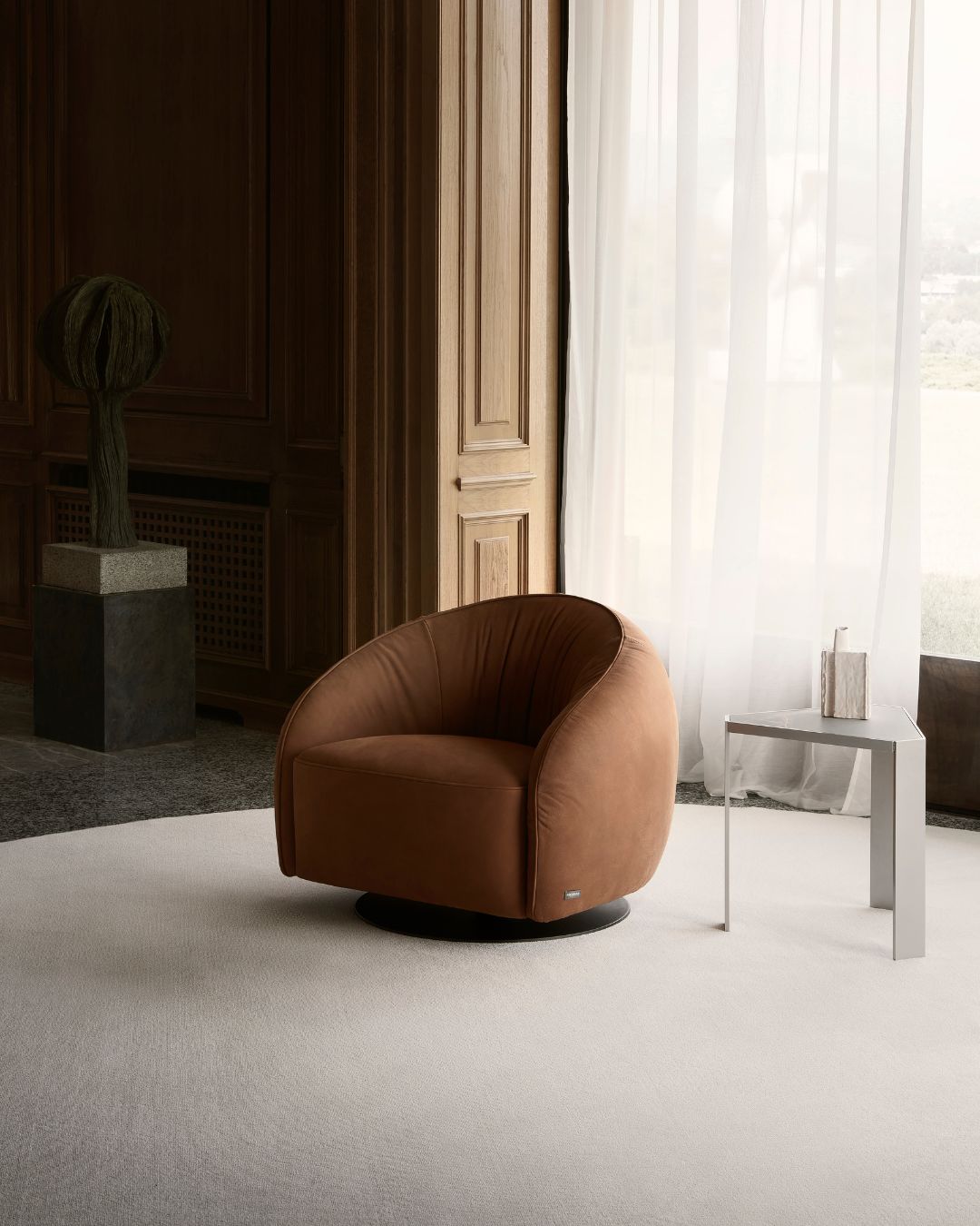 Nest fotelis iš Nicoline – apvalių, apgaubiančių formų, su žemu atlošu ir besisukančia baze