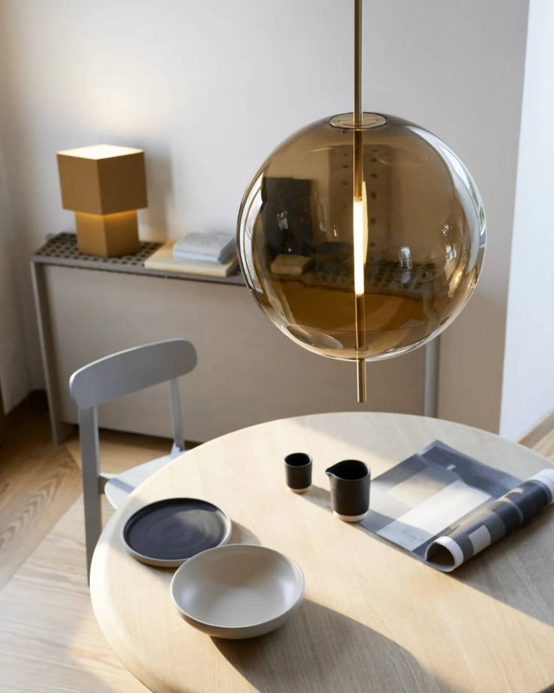 Burbulo formos pakabinamas šviestuvas su dūminto stiklo gaubtu minimalistiniame interjere virš valgomojo stalo