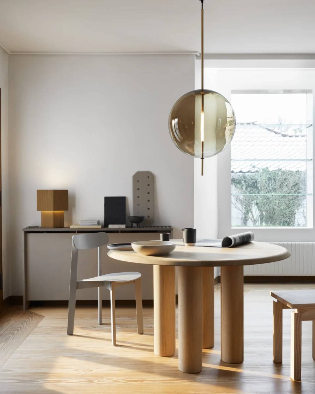 Burbulo formos pakabinamas šviestuvas su dūminto stiklo gaubtu minimalistiniame interjere virš valgomojo stalo