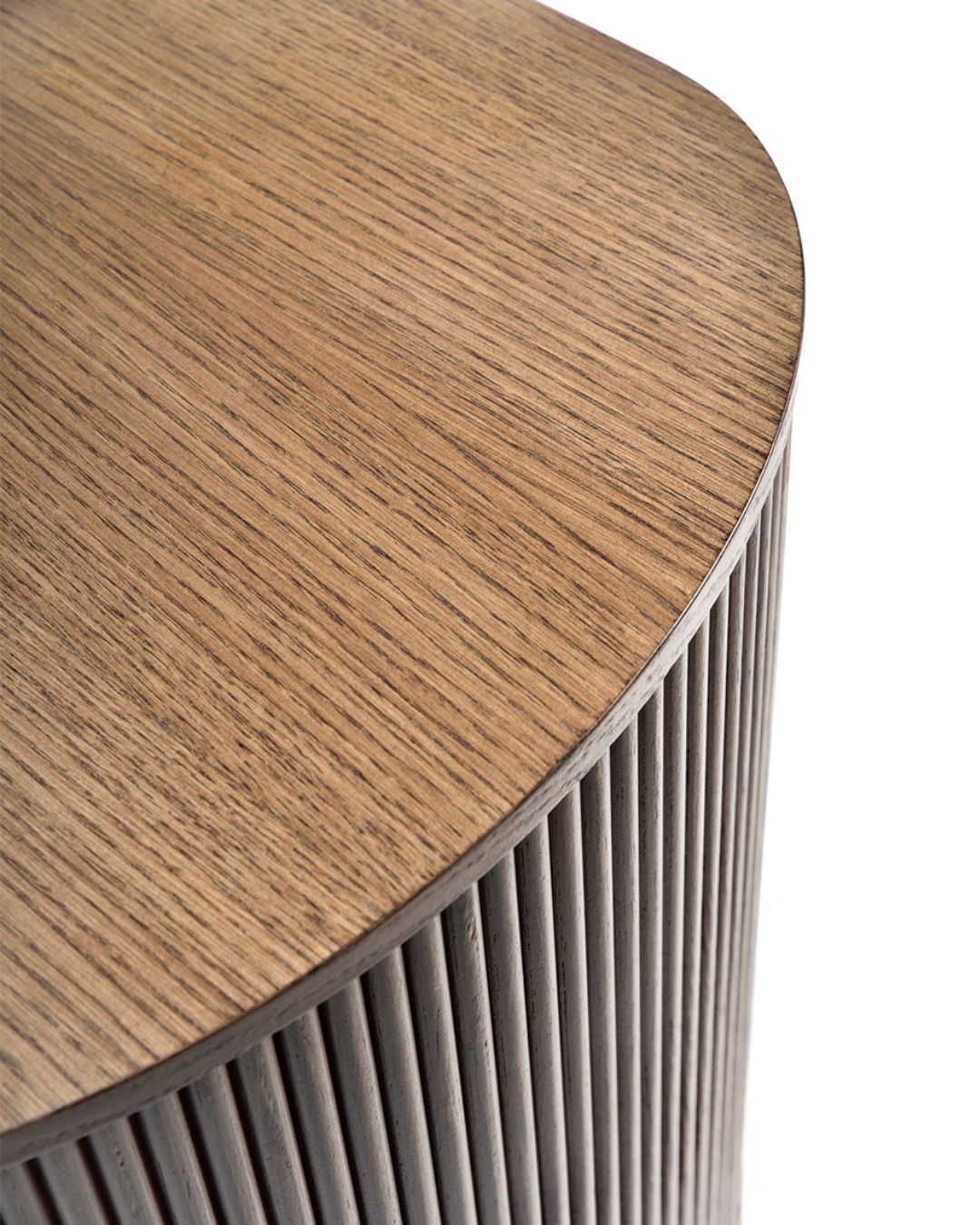 Ilga, minimalistinio dizaino medinė komoda su užapvalintais galais ir vertikaliu frezavimu fasade. Stovi ant plonų juodų metalinių kojelių, paviršius – šiltos riešuto spalvos.