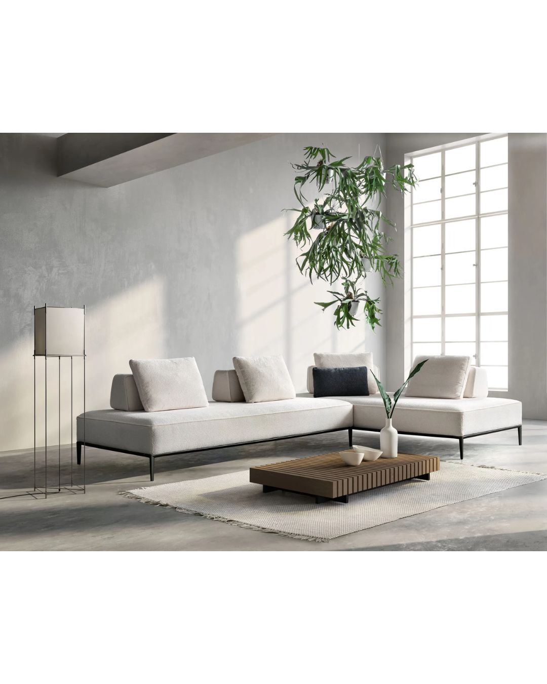 Kampinė baltos spalvos modulinė sofa aukštomis metalinėmis kojelėmis.