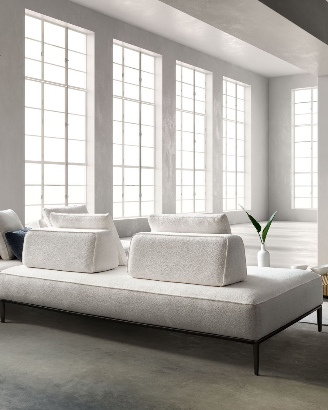 Kampinė baltos spalvos modulinė sofa aukštomis metalinėmis kojelėmis.