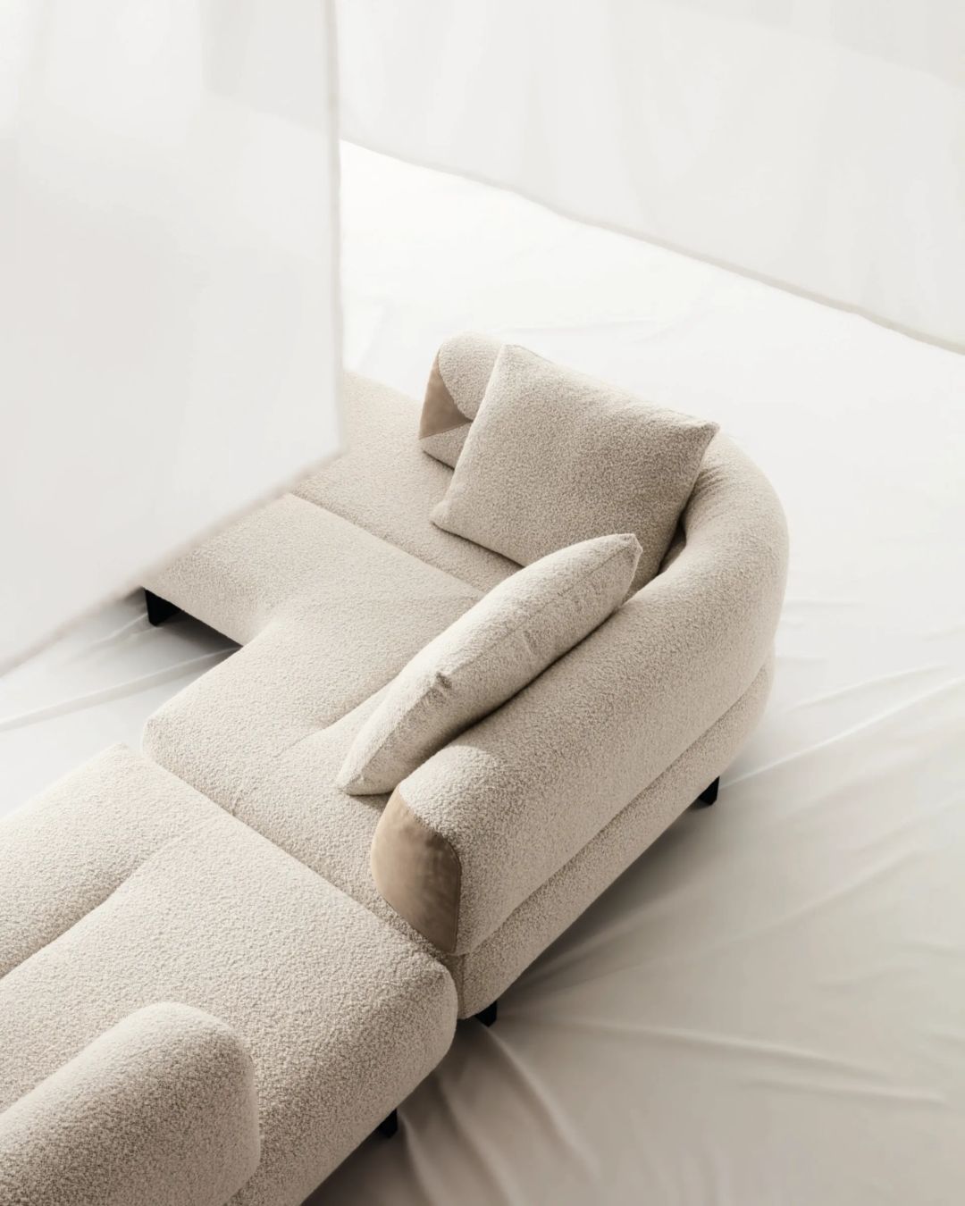 Šviesaus audinio sofa su lenktais porankiais ir juodomis metalinėmis kojelėmis. Nuotrauka šviesiame interjere.