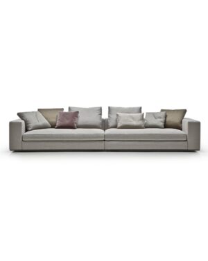 Didelė pilkos spalvos sofa su daug pagalvėlių. Nuotrauka baltame fone.